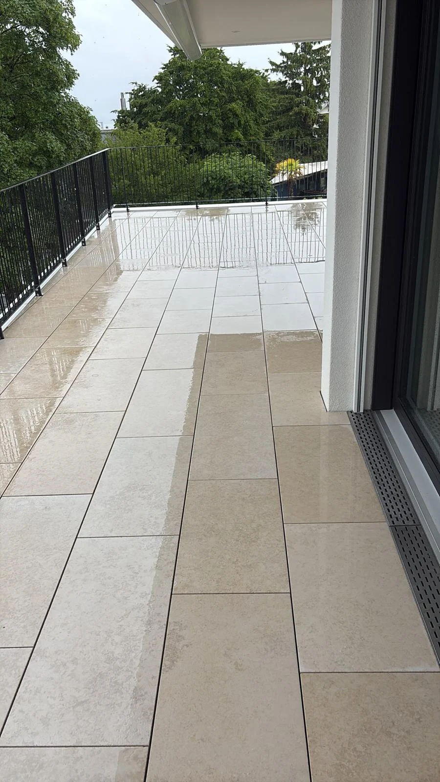 Auf der Terrasse liegen helle rechteckige Platten mit einer sichtbaren Entwässerungsrinne unmittelbar vor der Tür.