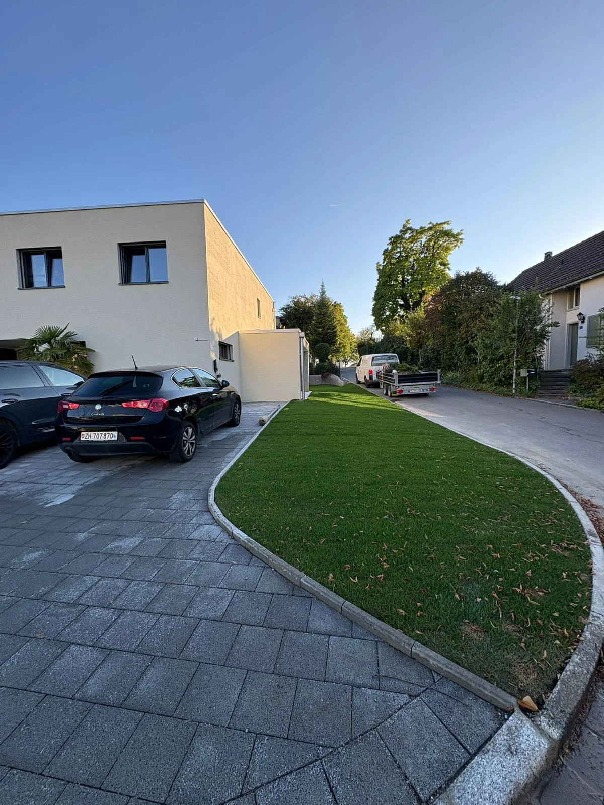 Geschwungene Raseninsel neben gepflasterten Stellplätzen